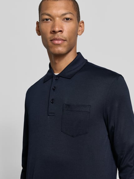 Männermodel trägt Regular Fit Poloshirt aus Baumwoll-Mix mit Brusttasche von bugatti, dunkelblau, Logo-Stickerei, Nahaufnahme Oberkörper.