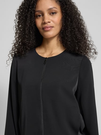 Modelka kobieca nosi Kurzblazer mit Rundhalsausschnitt od comma, czarny, krój regular fit, zamek z przodu, z elastycznego materiału, z wykończeniami, szerokość w rozmiarze 36: 54 cm, długość tyłu 50 cm, długość rękawa 63 cm, ujęcie: zbliżenie na górną część ciała.