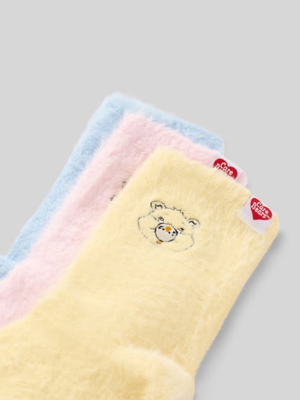 Produktfoto, Care Bear Socken mit elastischem Bund von adidas Originals in gelb, rosa und blau mit flauschiger Textur auf grauem Hintergrund