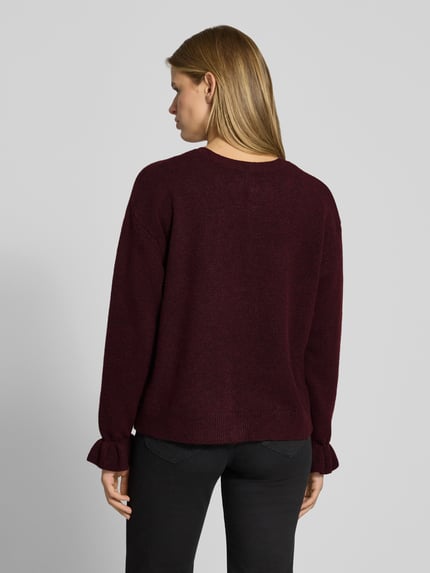 Frauenmodel trägt Strickjacke mit Schleifenverschluss Modell 'PCSALLY' von PIECES in bordeaux melange, strukturierte Strickoptik, Ganzkörperansicht Rückansicht.