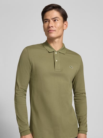Männermodel trägt Regular Fit Poloshirt aus reiner Baumwolle von Lacoste in Olivgrün, glatte Textur, Ganzkörperansicht von vorne, Herren Poloshirt von Lacoste.
