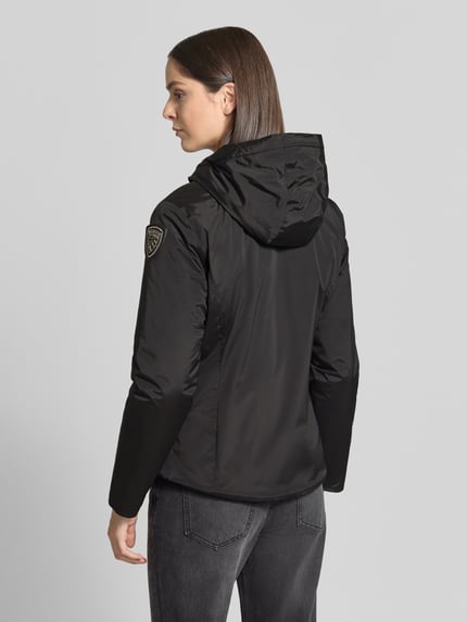 Frauenmodel trägt schwarze Regular Fit Jacke mit Logo-Detail Modell 'ERIE' von Blauer USA, glatte Textur, Ganzkörperansicht Rückansicht. Rückenlänge 63 cm, Schulterbreite 43 cm, Brustweite 50 cm, Ärmellänge 62 cm, Kapuze mit Tunnelzug, Zweiwege-Reißverschluss.