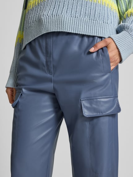 Frauenmodel trägt Straight Fit Hose in Leder-Optik mit Pattentaschen von Marc Cain, elastischer Bund, glatte Oberfläche, Nahaufnahme Oberkörper.