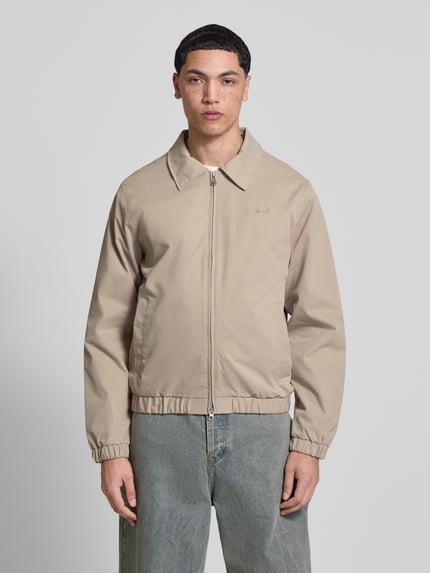 Männermodel trägt Jacke mit Zweiwege-Reißverschluss Modell 'CATSKILLS' von Jack & Jones in beige, regular fit, Umlegekragen, label-stitching, ganzkörperansicht von vorne, ruglengte maat M 64 cm, schouderbreedte 49 cm, borstwijdte 59 cm, mouwlengte 66 cm.