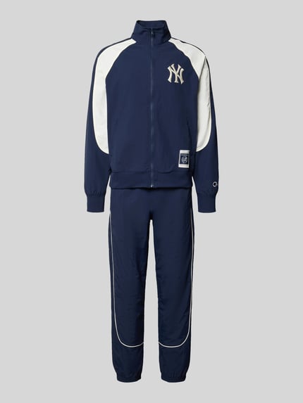 Produktfoto, Relaxed Fit Tracksuit mit Logo-Patch von Champion in dunkelblau mit weißen Kontrasteinsätzen, Reißverschluss, elastische Abschlüsse, sichtbarer Logo-Patch und NY-Schriftzug, Stehkragen, glatte Textur, alle Maße laut Größe M, sportlicher Look.