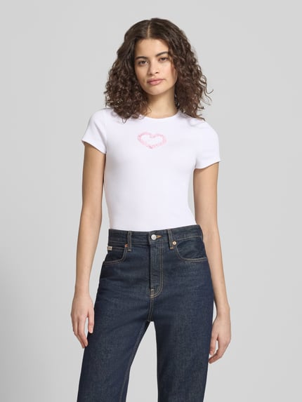 Modelka kobieca nosi damski t-shirt z mieszanki bawełny z dodatkiem streczu, prosty krój, model 'PREPPY HEART' od Review, okrągły dekolt, drobne prążkowanie, długość tyłu w rozmiarze S: 49 cm, kolor biały, gładka tekstura, całkowity widok z przodu.