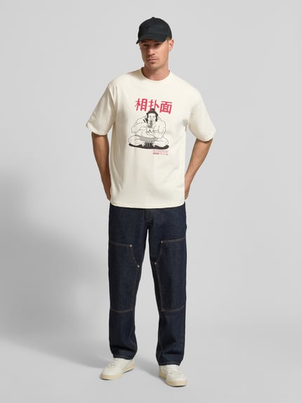 Männermodel trägt T-Shirt mit Motiv-Print Modell 'Baine' von WOODBIRD aus weißer Bio-Baumwolle, Regular Fit, Ganzkörperansicht von vorne.