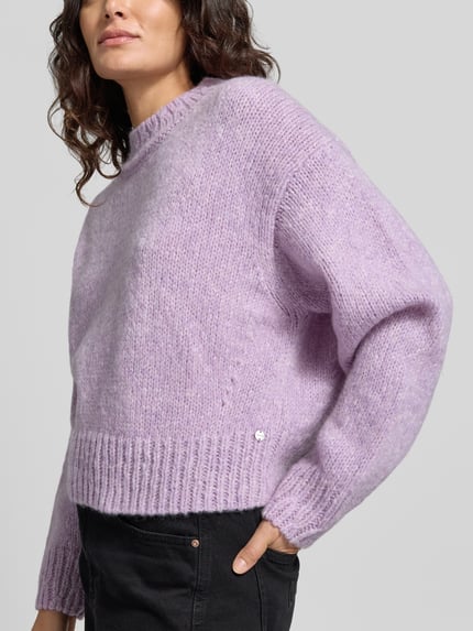 Modelka nosi sweter z alpaki i wełny z prążkowanymi ściągaczami Pullover aus Wolle Alpaka mit Rippbündchen od MARC CAIN, krój regular fit, jednokolorowy, imitacja dzianiny, długość krótka, opadające ramiona, okrągły dekolt, długie rękawy z prążkowanym wykończeniem, wykończenie dołu prążkowane, widok całego ciała z przodu.