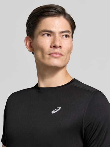 Męski model nosi Regular Fit T-Shirt mit Logo-Print von ASICS w kolorze czarnym, krój regular fit, okrągły dekolt, krótki rękaw, nadruk z logo, długość tyłu w rozmiarze M: 71 cm, zdjęcie: zbliżenie górnej części ciała.