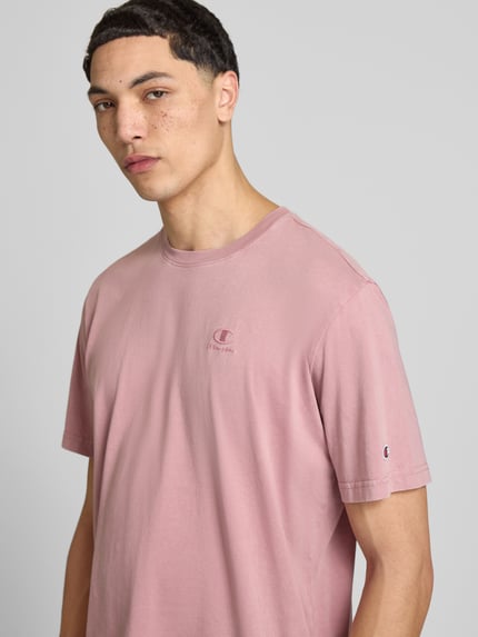 Männermodel trägt T-Shirt mit Label-Stitching und Rundhalsausschnitt von CHAMPION in Rosa, Reine Baumwolle, Regular-Fit, Nahaufnahme Oberkörper. Rückenlänge bei Größe M: 67 cm.