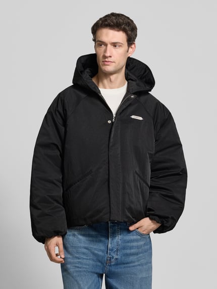 Männermodel trägt schwarze Relaxed Fit Bomberjacke mit Label-Patch Modell 'L’ATELIER' von RETERNITY, Eingrifftaschen, Kapuze, Ganzkörperansicht von vorne.