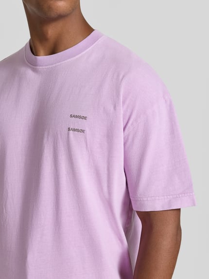 Männermodel trägt Oversized T-Shirt aus reiner Baumwolle Modell 'Joel' von Samsøe Samsøe in Flieder mit Logo-Print, Nahaufnahme Oberkörper.