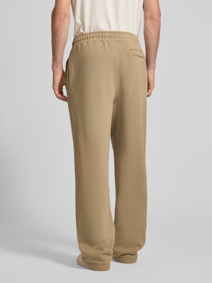 Männermodel trägt Loose Fit Sweatpants aus Baumwoll-Mix mit Label-Detail von PEGADOR in beige, elastischer Bund, Ganzkörperansicht Rückansicht.
