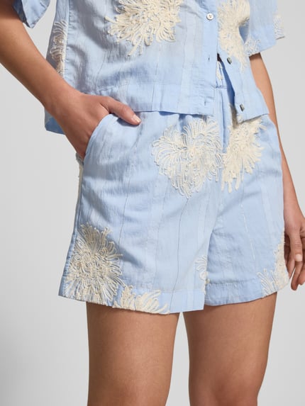 Frauenmodel trägt Straight Fit Shorts mit floralen Zierapplikationen Modell 'Kana' von YAS aus Reine Baumwolle, Nahaufnahme Oberkörper.