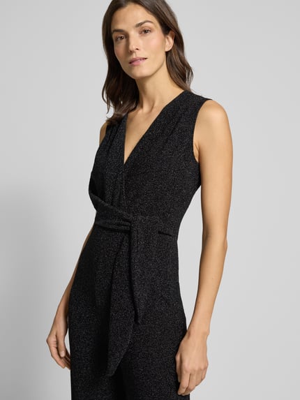 Kobiece modelka nosi Schimmernder Jumpsuit mit V-Ausschnitt od Rich & Royal, czarny połyskujący materiał, regularny krój, pasek w talii, zbliżenie na górną część ciała.