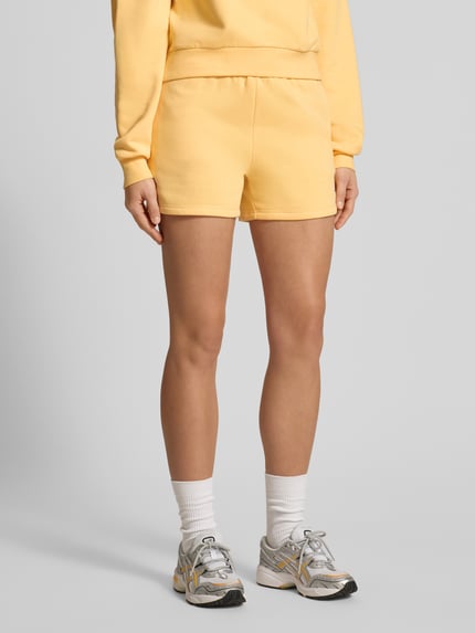Frauenmodel trägt Shorts mit Logo und elastischem Bund von adidas Sportswear aus gelbem Baumwoll-Mix, Regular Fit, Nahaufnahme Oberkörper.