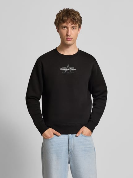 Männermodel trägt Regular Fit Sweatshirt aus Baumwoll-Mix mit Label-Detail von Alpha Industries, schwarze Farbe, Ganzkörperansicht von vorne. Rückenlänge bei Größe M 66 cm, elastische Abschlüsse, Nahaufnahme Oberkörper.