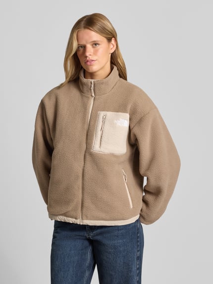 Frauenmodel trägt Jacke mit Wendefunktion Modell 'YUMIORI' von The North Face in Beige mit Stehkragen und Logo, Ganzkörperansicht von vorne, Regular Fit, Struktur aus Fleece, Rückenlänge 62 cm, Brustweite 57 cm, Schulterbreite 52 cm, Ärmellänge 57 cm.