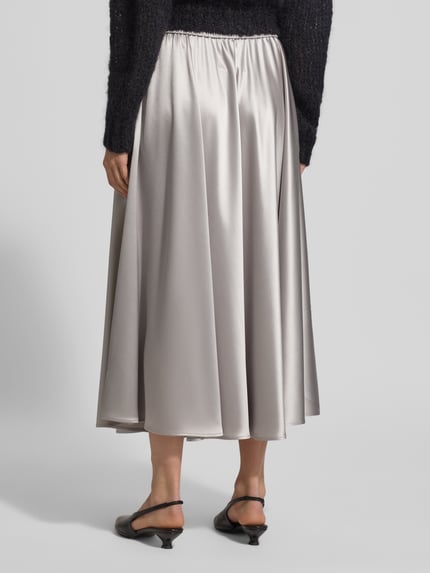 Frauenmodel trägt Midirock aus Satin mit elastischem Bund von HERZENS, A-Linie, fließender Stoff, silbergraue Farbe, Ganzkörperansicht Rückansicht.