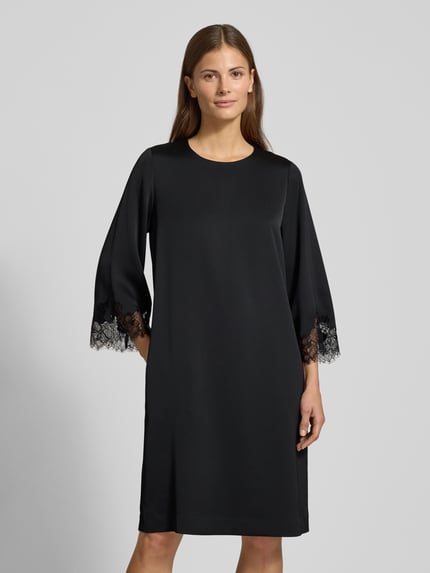 Kobiece model nosi sukienkę knielange Kleid mit Rundhalsausschnitt Modell 'Dancia' od JOOP!, krój relaxed fit, okrągły dekolt, długość do kolan, rękaw o dł. 3/4 z obszyciem koronką, długość tyłu 100 cm, szerokość klatki piersiowej 49 cm, długość rękawa 65 cm, gładka czarna tkanina, widok całej sylwetki z przodu.