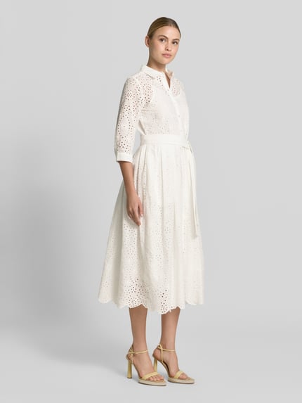 Vrouwenmodel draagt overhemdjurk uit broderie met knoopsluiting van Milano Italy, puur katoen, getailleerd model, midi-jurk, overhemdkraag, strikceintuur, ruglengte maat 36: 121 cm, borstwijdte maat 36: 41 cm, mouwlengte maat 36: 38 cm, wit met ronde vormen en lichte textuur, geheelvooraanzicht.