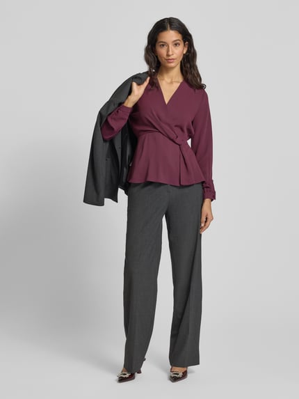 Frauenmodel trägt Regular Fit Bluse mit Knoten-Detail von Rinascimento in Dunkellila, V-Ausschnitt, graue Hose, Ganzkörperansicht von vorne.