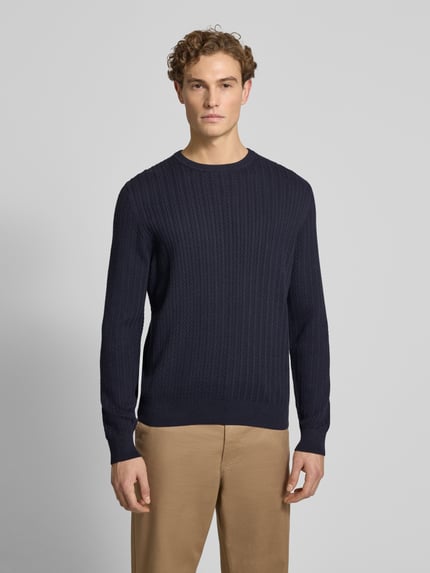 Męski model nosi Strickpullover mit gerippten Abschlüssen od Christian Berg Men, bawełna, granatowy, okrągły dekolt, regular fit, widok z przodu całej sylwetki.