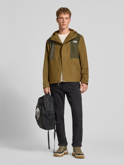 Mężczyzna nosi kurtkę z kapturem Jacke mit Label-Stitching Modell 'REIGN ON 2.0' od The North Face, krój regular fit, oliwkowe odcienie, zamek błyskawiczny ukryty, szerokość ramion w rozmiarze M 52 cm, szerokość klatki piersiowej w rozmiarze M 63 cm, długość rękawów 65 cm, długość tyłu 69 cm, widok całej sylwetki z przodu.