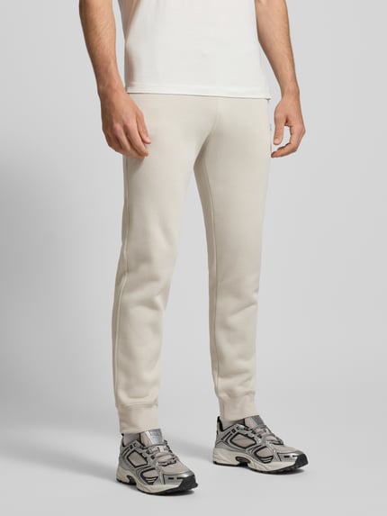 Männermodel draagt Sweatpants mit elastischem Bund und Label-Stitching van CHAMPION in beige, katoenmix, regular fit, binnenbeenlengte 76 cm, labelstitching detail, vooraanzicht tot op de enkels.