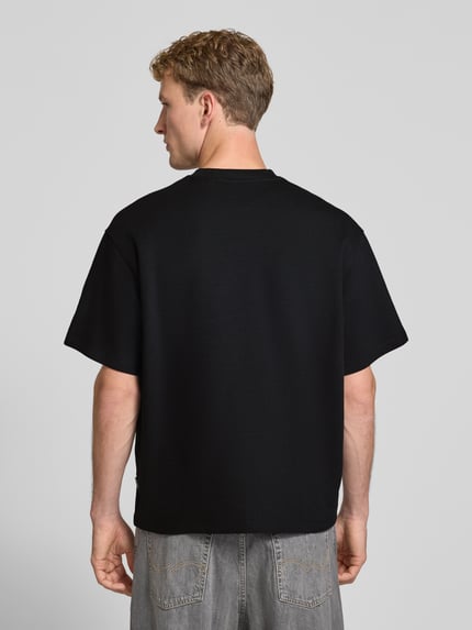 Männermodel trägt schwarzes Relaxed Fit T-Shirt aus elastischem Baumwoll-Mix Modell 'SCUBA' von JACK & JONES, Produktkontext sichtbar, Ganzkörperansicht Rückansicht.