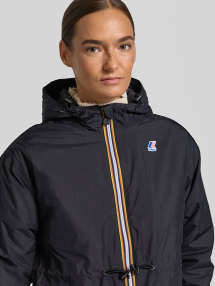 Frauenmodel trägt Regular Fit Mantel mit Logo-Print Modell 'DELIA' von K-WAY in Schwarz, Kapuze mit Tunnelzug, Nahaufnahme Oberkörper.