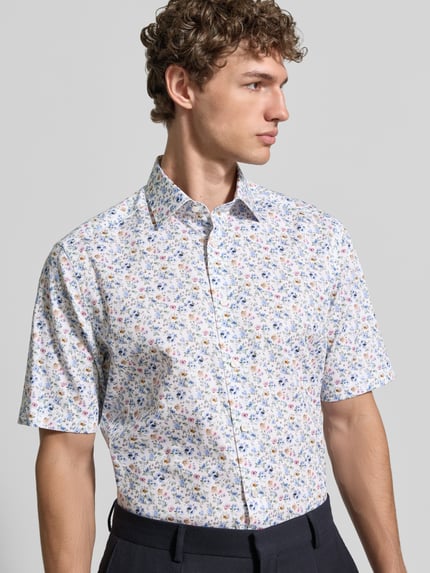 Männermodel trägt Regular Fit Freizeithemd mit Kentkragen von OLYMP, floraler Allover-Print, durchgängige Knopfleiste, kurzärmelig, Ganzkörperansicht von vorne.