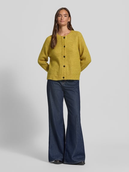Frauenmodel trägt Relaxed Fit Strickjacke aus Woll-Mix Modell 'LULU' von Selected in Gelb, kombiniert mit blauer Jeans, Ganzkörperansicht von vorne. Damen Strickjacke von Selected.