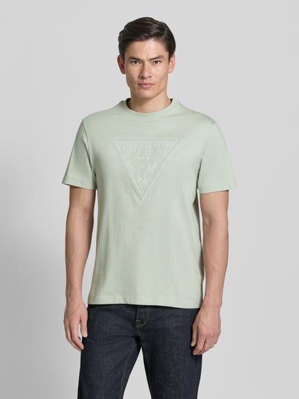 Männermodel trägt T-shirt met logoprint en ronde hals 'T-shirt met logo en ronde hals' van guess, puur katoen, regular fit, ruglengte maat M 70 cm, lichte groentint, gladde textuur, Ganzkörperansicht van voren.