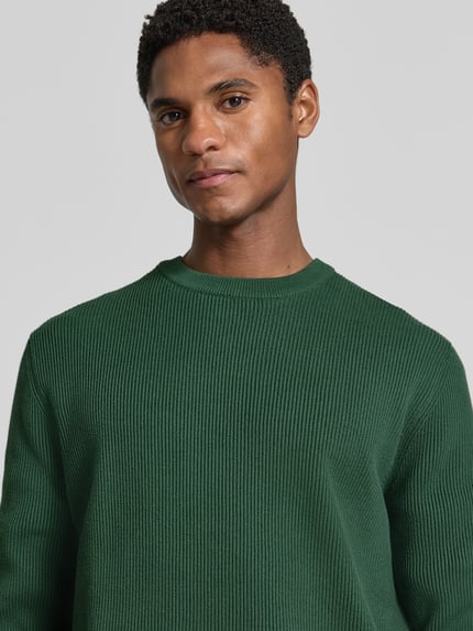 Männermodel trägt Slim Fit Strickpullover Baumwoll-Mix von Lindbergh in Dunkelgrün, gerippte Optik, Nahaufnahme Oberkörper.