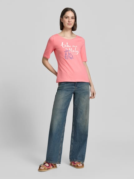 Kobiece modelka nosi damski t-shirt Regular Fit T-Shirt aus Baumwoll-Mix mit Motiv-Print von Tom Tailor, efekt: jednolity kolor, krój regular fit, nadruk z motywem, okrągły dekolt, krótki rękaw, mieszanka bawełny, Ganzkörperansicht von vorne.