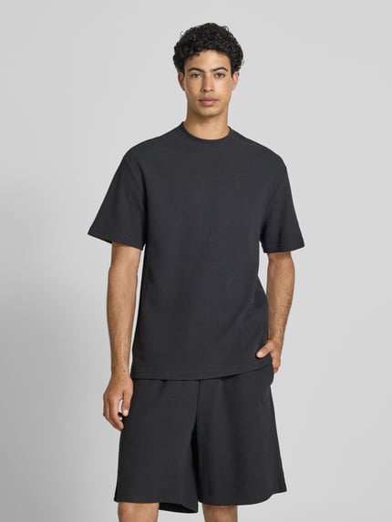 Männermodel trägt Oversized T-Shirt mit Strukturmuster und Logo-Stitching von KARL KANI aus Baumwoll-Mix, schwarze Farbe, Rundhalsausschnitt, Oversized-Fit, Herren T-Shirt, Rückenlänge 75 cm, Ganzkörperansicht von vorne.