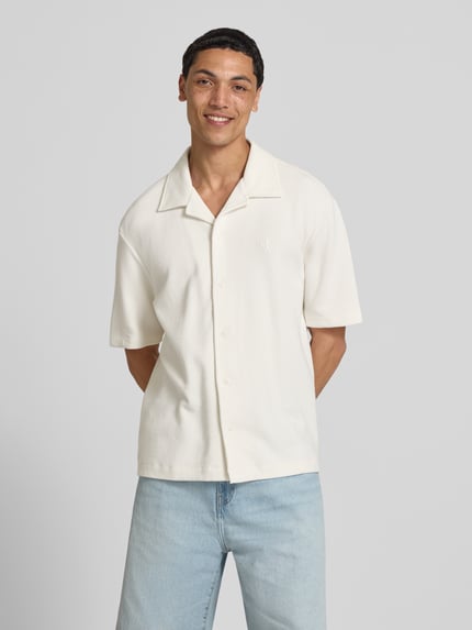 Männermodel trägt Relaxed Fit Freizeithemd aus reiner Baumwolle von Calvin Klein Jeans, Optik: Unifarben, Ärmelform: Kurzarm, Materialverarbeitung: Piqué, Logo-Stitching, Reverskragen, durchgehende Knopfleiste, Ganzkörperansicht von vorne.