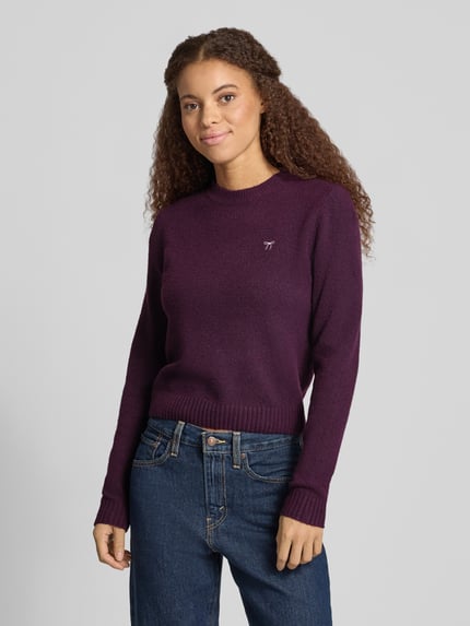 Modelka nosi Slim Fit Strickpullover aus elastischem Material-Mix od REVIEW, elastyczna mieszanka materiałów, krój slim fit, wyhaftowany motyw, prążkowane wykończenia, długość tyłu w rozmiarze S: 51 cm, długość rękawów w rozmiarze S: 61 cm, kolor ciemnofioletowy, prosta forma, gładka tekstura, widoczne prążkowane ściągacze, widok na górną część ciała z przodu.