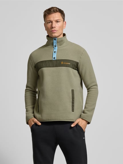Męski model nosi Sweatshirt mit Label-Print od Cotopaxi w luźnym kroju, kolor oliwkowy, kieszenie, krótka listwa napy, przód, ujęcie całego ciała.