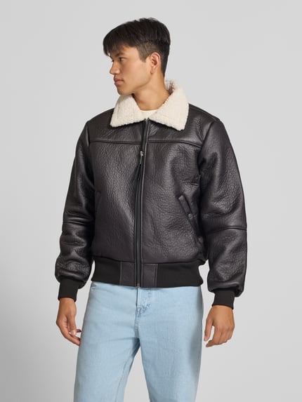 Männermodel trägt schwarze Bomberjacke mit Kentkragen und gerippten Abschlüssen von Alpha Industries, beige Teddyfell, Vorderansicht, Nahaufnahme Oberkörper. Herren Bomberjacke mit Reißverschluss, Eingrifftaschen mit Druckknopfverschluss, Regular Fit, Maße: Rückenlänge 66 cm, Schulterbreite 48 cm, Brustweite 55 cm, Ärmellänge 70 cm.