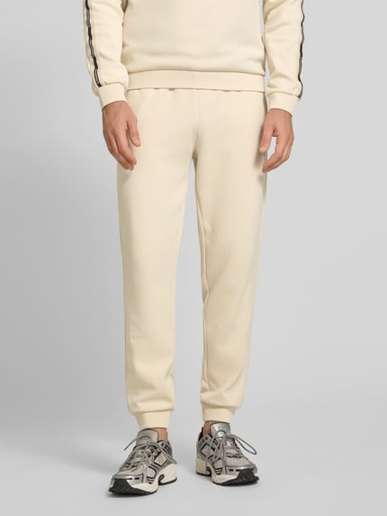 Męski model nosi Sweatpants aus Baumwoll-Mix od EA7 Emporio Armani, mieszanka bawełny i elastanu, luźny krój, elastyczny pas z tunelem, elastyczne zakończenia nogawek, wpuszczane kieszenie, długość wewnętrzna nogawki w rozmiarze m: 78 cm, jasny kolor, gładka tekstura, całkowity widok z przodu