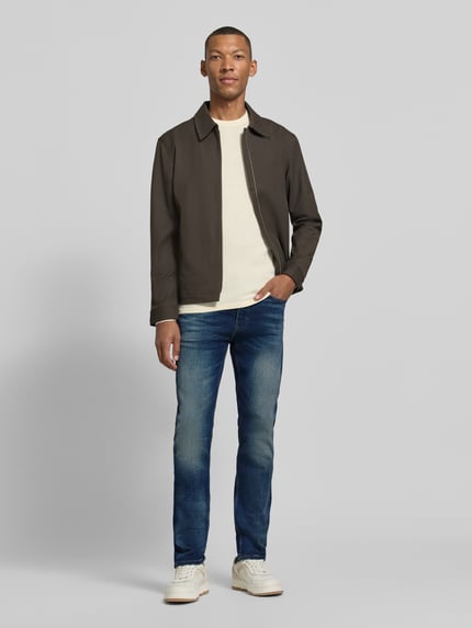 Männermodel trägt Slim Fit Jeans mit Label-Patch Modell 'DELAWARE BO' von BOSS Orange, mittleres Blau, Used Look, Ganzkörperansicht von vorne.