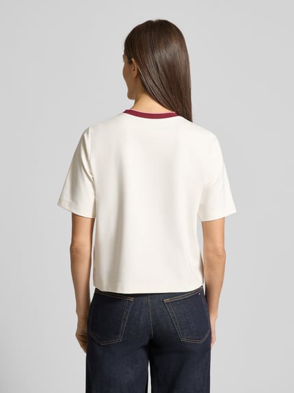 Frauenmodel trägt Regular Fit T-Shirt mit Strasssteinbesatz von Marc Cain, cremefarben, elastischer Baumwoll-Mix mit Modal-Anteil, Rundhalsausschnitt, Ganzkörperansicht Rückansicht.