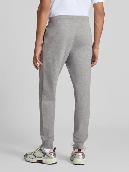 Männermodel trägt graue Sweatpants mit Label-Print Modell 'GORDON' von JACK & JONES, lockere Passform, Rückansicht, Ganzkörperansicht.