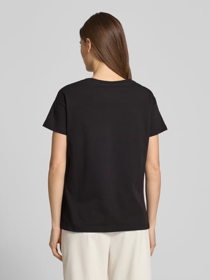 Vrouwenmodel draagt T-Shirt aus reiner Baumwolle van ARMANI EXCHANGE in zwart, rechte fit, ronde hals, labeldetail, strass-steentjes, ruglengte maat S 59 cm. Volledige lichaamsweergave achteraan.