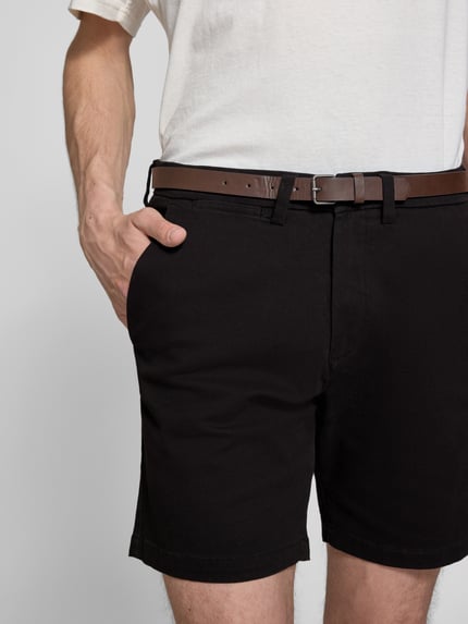 Männermodel trägt Straight Fit Shorts mit abnehmbarem Gürtel Modell 'Adam' von Jack & Jones, schwarze Baumwoll-Mix-Textur, Nahaufnahme Oberkörper. Elastischer Bund, Eingriffstaschen, Knopf- und Reißverschluss, Bundweite 40 cm, Innenbeinlänge 19 cm.