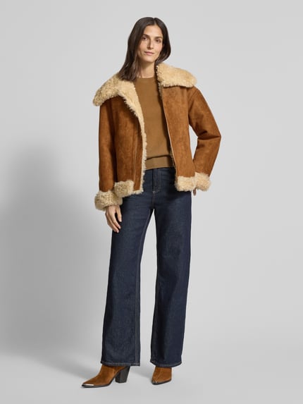 Frauenmodel trägt Jacke mit Futter aus Teddyfell Modell 'ADRIANA' von Mango, Relaxed-Fit, Umlegekragen, Reißverschluss, Eingrifftaschen, braune und beige Farben, samtige und weiche Textur, Ganzkörperansicht von vorne. Rückenlänge 63 cm, Schulterbreite 52 cm, Brustweite 56 cm, Ärmellänge 55 cm.