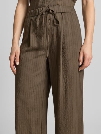 Frauenmodel trägt Stoffhose aus Viskose-Mix Modell 'TATU' von Mango in Braun, Wide Leg, elastischer Bund, Nahaufnahme Oberkörper.