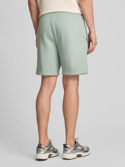 Männermodel trägt Sweatshorts mit Logo und elastischem Bund von GAP aus mintgrünem Baumwoll-Mix mit Eingrifftaschen, Regular-Fit, Ganzkörperansicht Rückansicht.